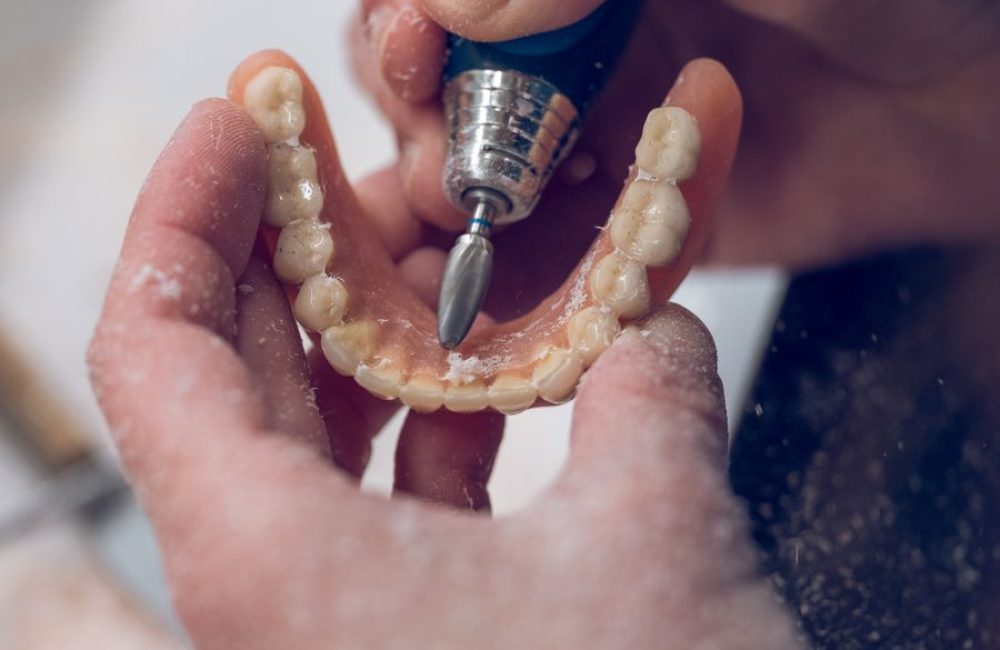 Crop person polishing implants of jaw of denture From above of crop anonymous female grinding with rotary machine non removable prothesis while working in laboratory